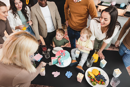 Cake-cutting activity at a gender reveal celebration. A young Caucasian expectant mother cutting a cake to find out the baby's gender while her supportive friends are surrounding her. Exciting moment of revealing that the baby is a boy.