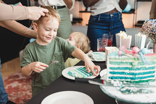 Happy young Caucasian sibling about to eat some delicious blue cake at a celebration. They are enjoying their birthday party and look happy.