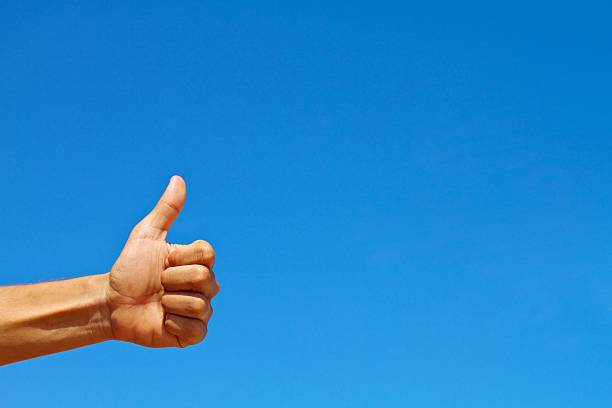 Thumbs up symbol against blue sky stock photo