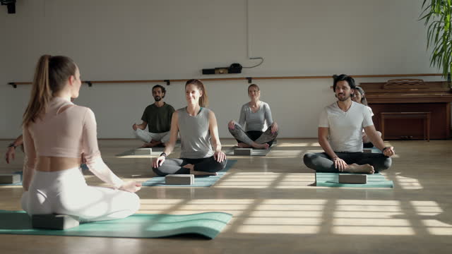 Caucasian Young Female Yoga Teacher Sitting In Front Of Their Students And Talking To Them Before Beginning The Class