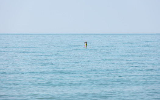 Distant unrecognizable woman on a SUP board floating on a stand up in the sea. Concept lifestyle sport and meditation
