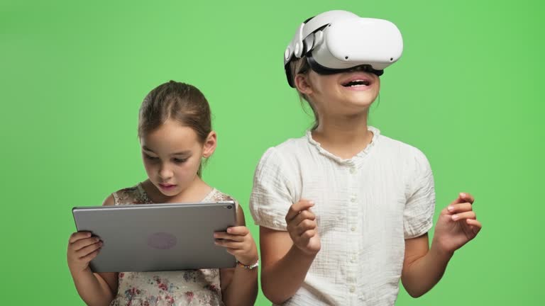 Portrait of a happy child girls with virtual reality simulator headset and digital tablet on green background