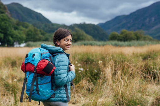 Girl on a hike outdoors in Keswick, Lake District. She is smiling looking over her shoulder at the camera holding a backpack.