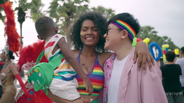 Happy multiracial family spending cheerful moment together in pride parade event near seaside, LGBTQ lesbian parents and son embracing each other to support diversity