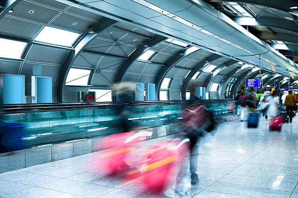 Travellers Walking Down Corridor passengers rushing through airport tunnel, pulling luggage, long exposure, blurred motion business architecture blue people stock pictures, royalty-free photos & images