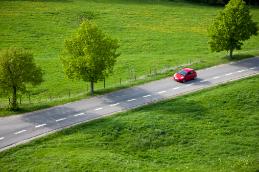 small red car driving down country road, springtime, elevated view,