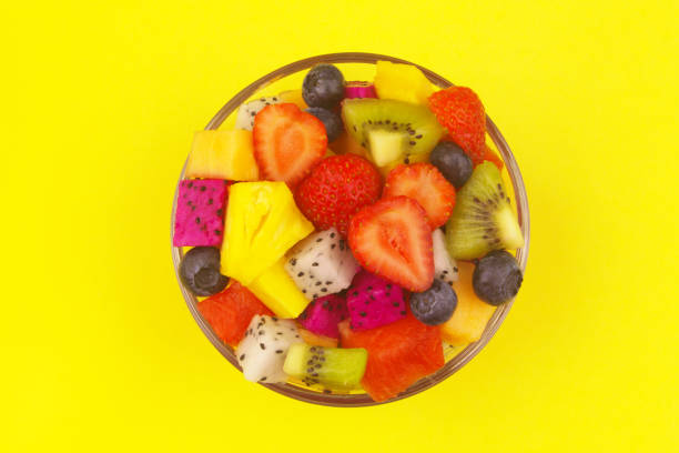 Top view of bowl with fruit salad on yellow background.