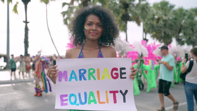 LGBTQ lesbian women holding marriage equality banner in pride parade event to support equality and human rights, African LGBTQ women smiling and celebrating in pride event on street near seaside