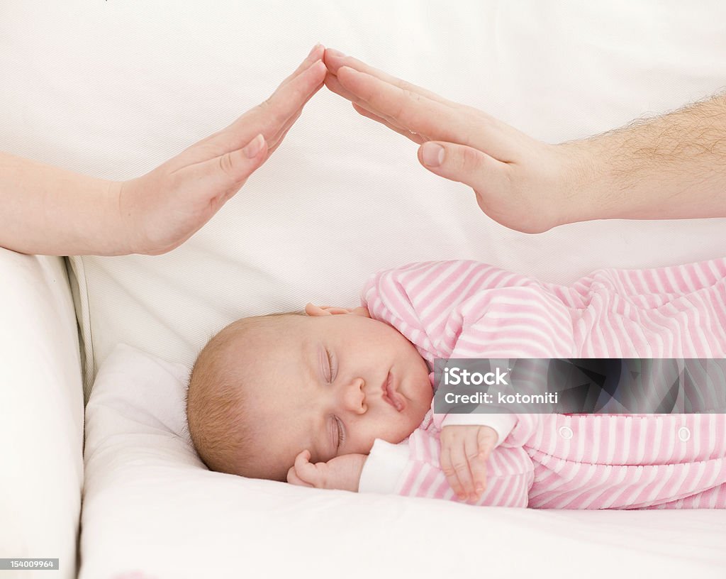 sleeping baby Hands of parents combined by a small house over the sleeping baby. The concept of care of children. Baby - Human Age Stock Photo