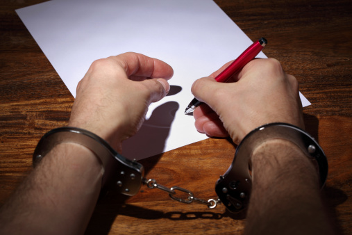 Man in handcuffs signing a document concept for coercion or being pressured into giving a signature or marriage