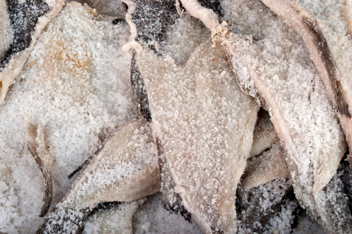 Close up of a large number of salted cod fish fillets in a market.  This is traditional European food and is called Bakalarou in Greece.  White fish, especially cod, is dried and preserved by adding salt to it.  One can see the large amount of salt on these cod fish.