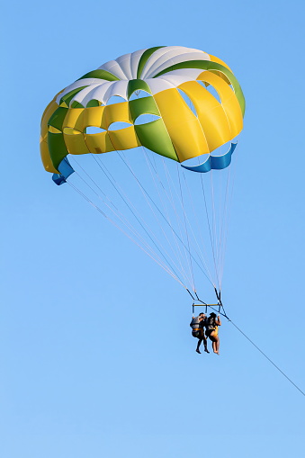 Fiumefreddo di Sicilia, Sicily, Italy - August 12, 2022 A black couple in bathing suits and life jackets pulled and flying with a yellow parachute near the shore