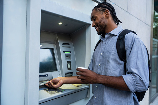 Medium shot portrait of African American man depositing money on ATM while standing on street