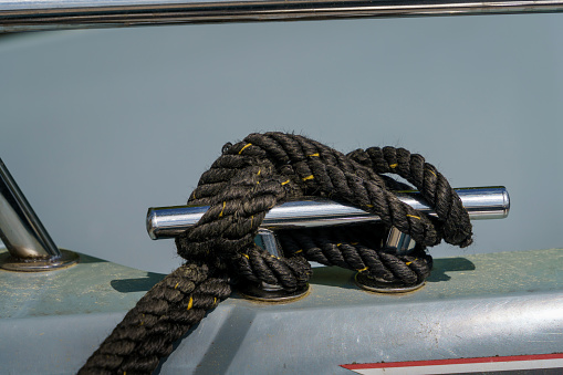 Black rope tied to the mooring cleat of a boat, close up.
