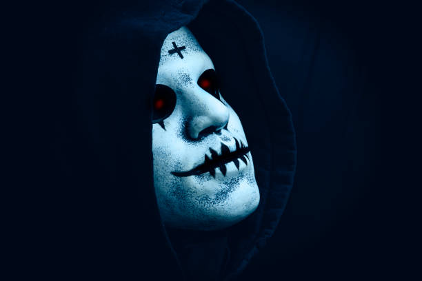 A side view of a creepy Halloween face mask in a hood with red glowing eyes.