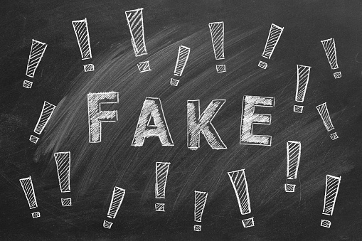 The word FAKE and exclamation marks written in chalk on a blackboard. Information and disinformation concept. Fake news. Hand drawn illustration.