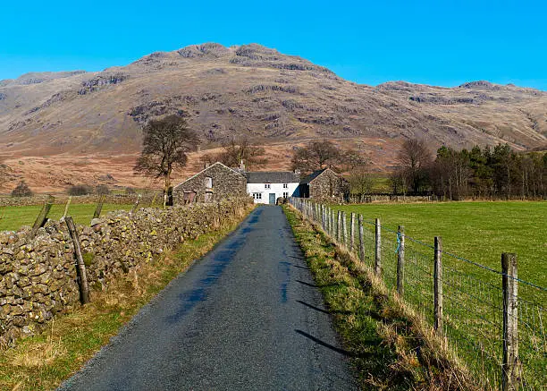 An English country road in the Duddon Valley, Cumbria, with a white cottage at the end of the road.
