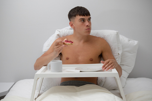 Young single shirtless man having breakfast in bed