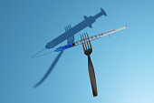 Medical syringe with medicine poked by a silver fork on blue background. Illustration of the concept of food medicine and relationship between food and medicine such as allergies, diabetes, obesity