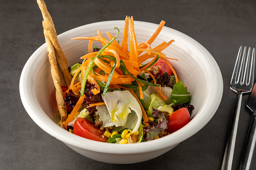 Salad with carrots, tomatoes, corn and lots of greens on a white porcelain plate