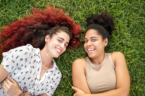 Cheerful multi-ethnic best friends lying on the grass in a park laughing in fun