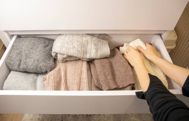 женщина складывает теплую одежду в белый шкаф. женские руки крупным планом. организация домашнего хранения - cardigan стоковые фото и изображения