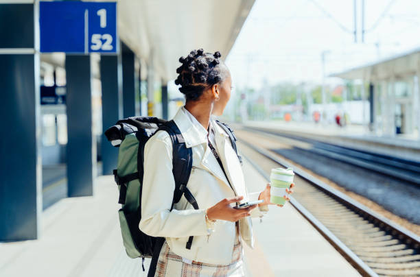 istock Woman with afro hair using smartphone while wait for her train on the railway station platform. Tourism and travel in the summer. Vacations for the student. Work and travel. 1540302973