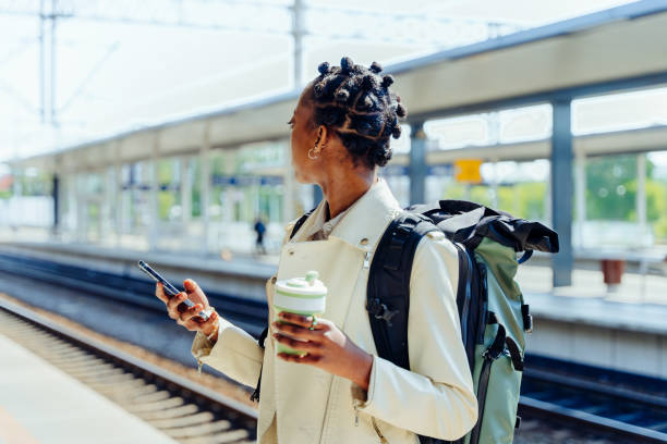 istock Black woman with back pack using smartphone and looking at arriving train at a railway station. Tourism and travel in the summer. Vacations for the student. Work and travel. Public transport concept. 1540302982