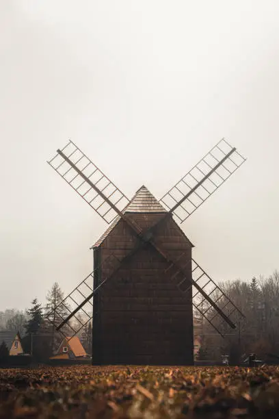 Photo of Ancient wooden mill standing alone in a field in gloomy foggy weather. Historical building for grinding corn, Opava, Czech Republic