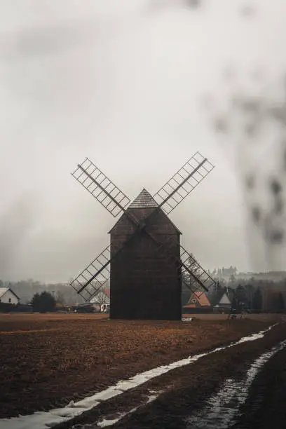 Photo of Ancient wooden mill standing alone in a field in gloomy foggy weather. Historical building for grinding corn, Opava, Czech Republic