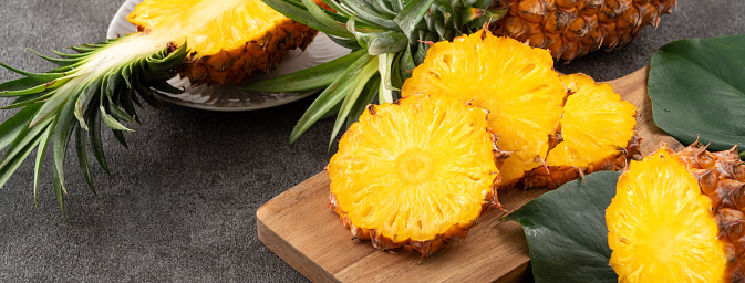 Fresh cut sliced juicy pineapple in a plate over dark gray table background.