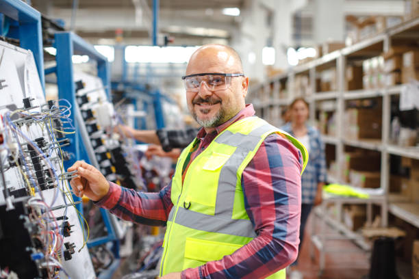 Joyful Work: Smiling Mature Manual Worker Man at Manufacturing Factory Discover the joy and contentment on the face of a mature manual worker as he carries out his duties at a manufacturing factory. This captivating portrait captures his genuine smile, reflecting his satisfaction and fulfillment in his work. Witness the dedication and experience that shines through his eyes in this vibrant image." manufacturing occupation stock pictures, royalty-free photos & images