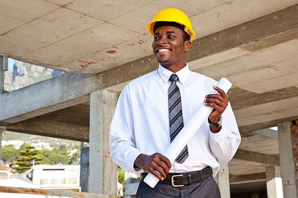 Portrait of an African man in a building site wearing a hard hat holding building plans