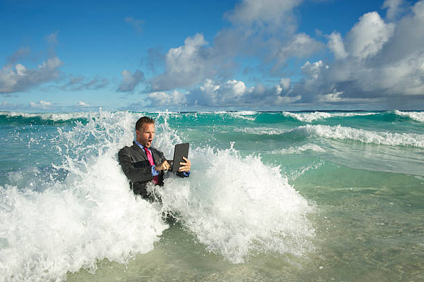 homme d'affaires en utilisant une tablette dans les vagues de la mer - computer humor stranded business photos et images de collection