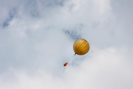 orange weather balloon with attached parachute, released against a cloudy sky by the National Weather Service, Dulles Virginia