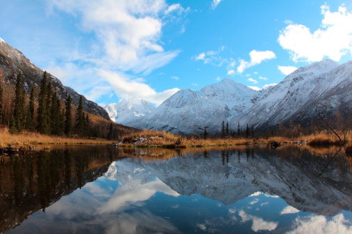First Snow on mountains in the Chugach State park in Eagle River, Alaska with reflection of sky in pond and fall colors