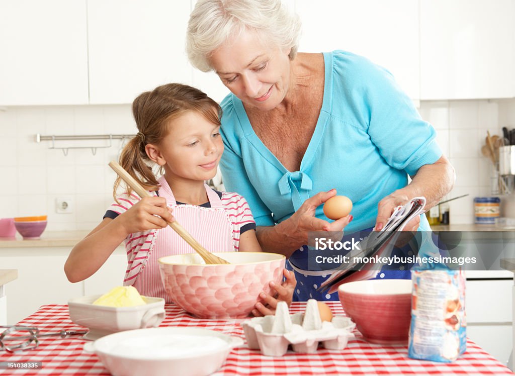 Grandmother And Granddaughter Baking In Kitchen Grandmother And Granddaughter Baking In Kitchen Reading Recipe Book. Adult Stock Photo