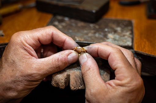 Goldsmith man working in his crafting jewelry workshop repairing and creating a gold ring with a diamond in his work studio. Jeweler mal holding a wedding ring. Jewel, craft and luxury concept.