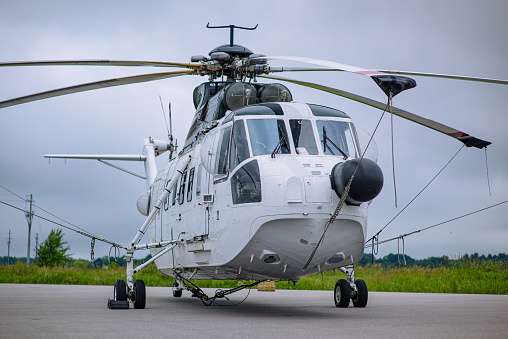 A twin engine single rotor heavy lift helicopter parked on a helipad.  Set against a grey overcast sky.