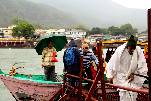 Rishikesh, Uttarakhand, India –  May 03, 2023 : Group of people crossing holy River Ganges in motorboat during rainy season.