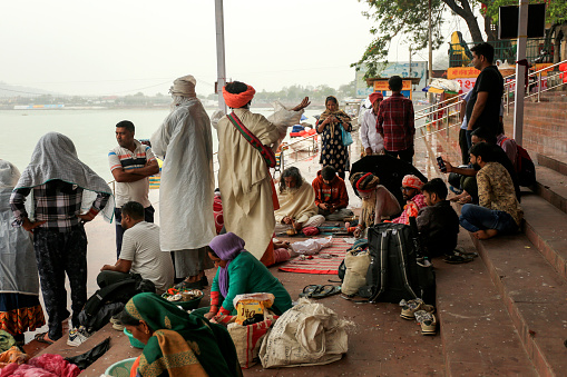 Rishikesh, Uttarakhand, India –  May 03, 2023: Group of people sitting near Holy River Ganges during rainy season.