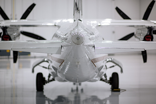 A white turboprop aircraft sits inside a hangar. The image is focused on the read strobe and tail of the aircraft. The background and wings are out of focus.