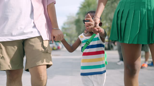 Mother and Father holding African son hands and walking on street near beach, Happy multiracial family spending time together, Cheerful child wearing sunglasses having happy moment