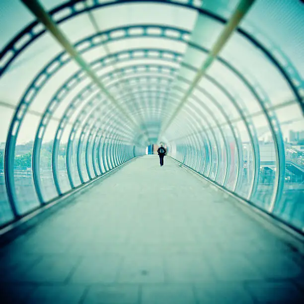 Lonely man walking inside glass tunnel, tilt shift