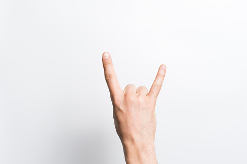 A close-up of a man's hand shows a punk or rock gesture isolated on a white studio background. The horns symbol. Heavy metal concept.