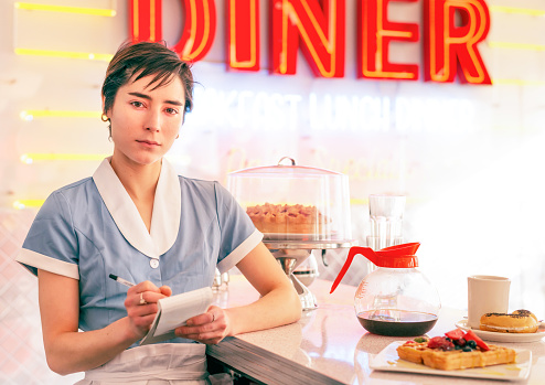 A young woman ready to take food and drinks orders at a diner.