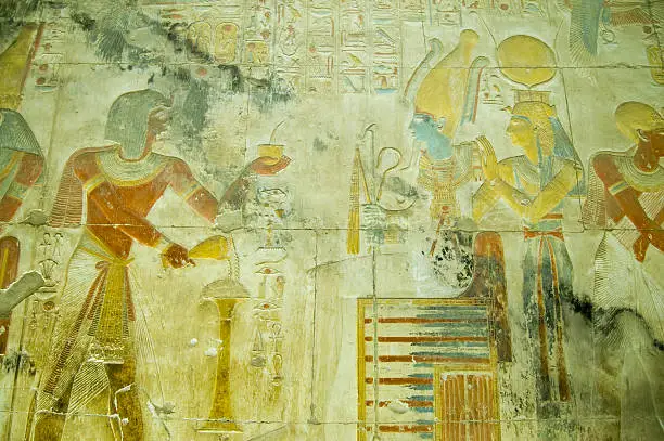 Ancient Egyptian bas relief carving showing the Pharaoh Seti I making an offering of incense to the god of the underworld Osiris with his wife, the goddess Isis standing behind.  