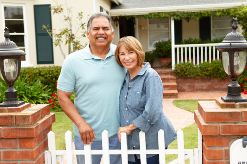 Senior Hispanic couple standing outside home smiling