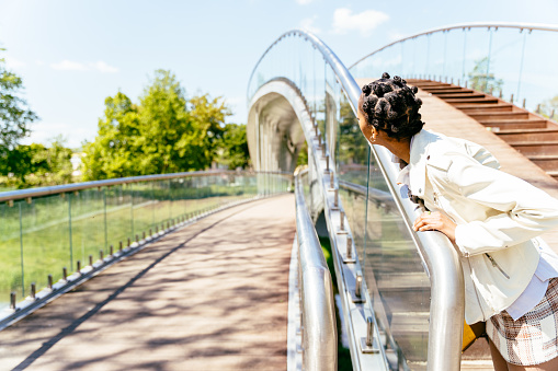 Beautiful african woman walking and admiring of a modern metal pedestrian bridge and looking at city park.