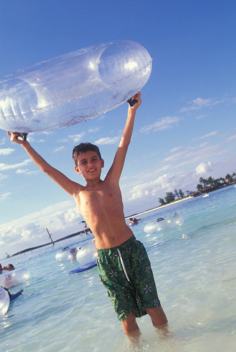 Boy lifting an inflatable swim ring on the beach, smiling portrait, Bahamas